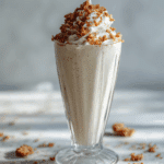 Vanilla milkshake in tall glass with whipped cream and cookie crumble topping