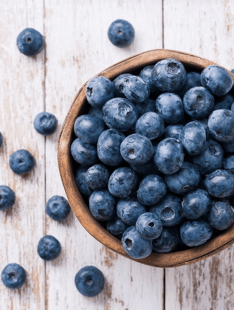 A rustic wooden bowl filled with fresh blueberries on a white wood background