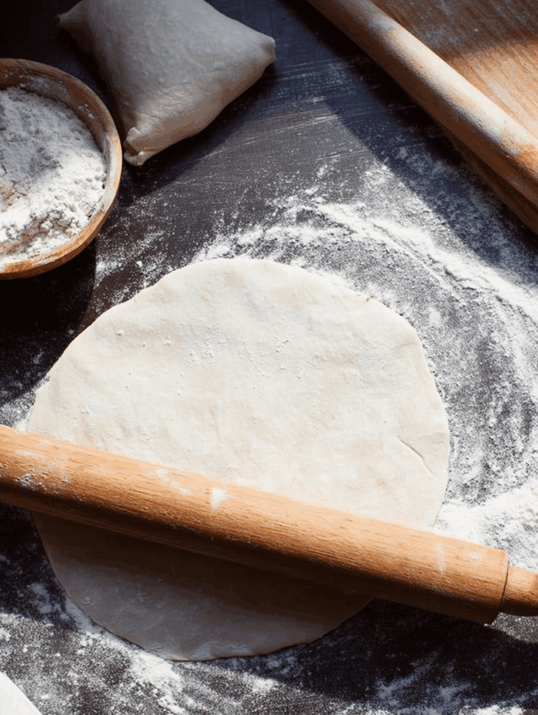 Rolled dough circle with flour and rolling pin on a dark counter